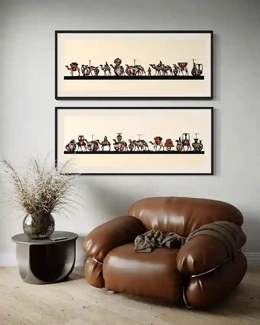 Two framed art prints of camel caravan, by Yousif Ibrahim and white wall behind a brown leather armchair in a room. UAE