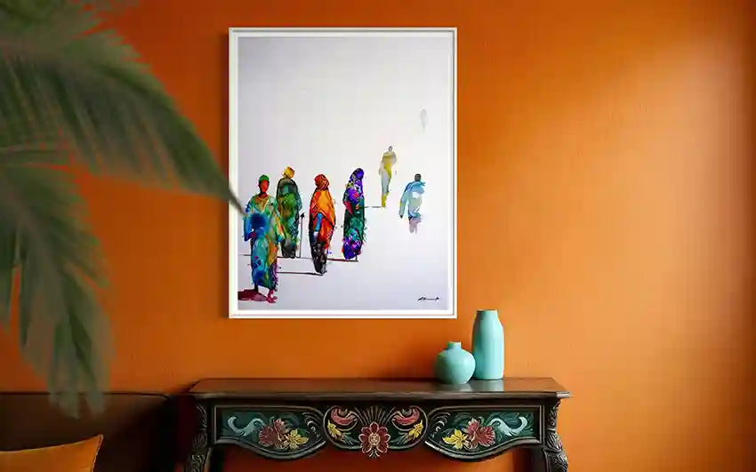 Framed art print of colorful figures on an orange wall with a decorative table below. by Visual Sudanese artist Galal Yousif, in UAE