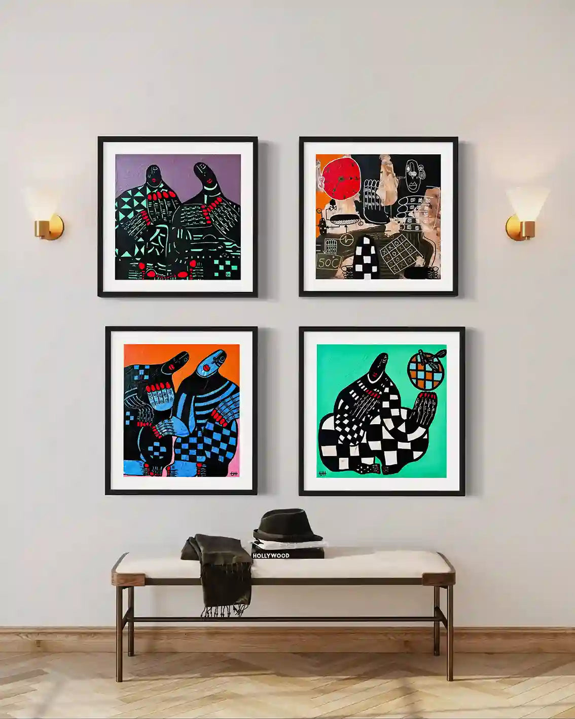Four original artworks by Usra Hamza in black frames on wall with brass sconces above bench with hat and scarf