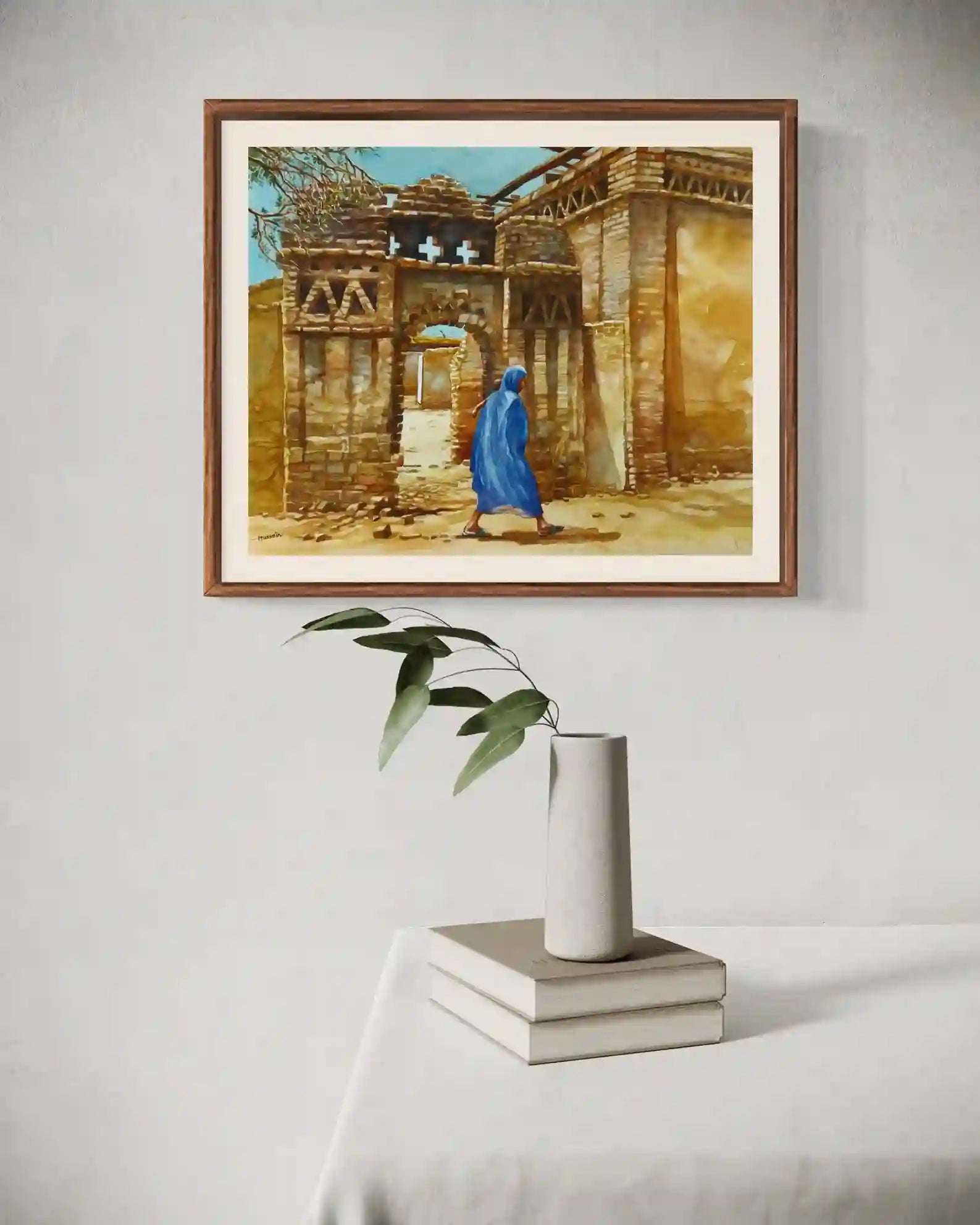 Nubian Echoes framed watercolor by Hussein Merghani above white books and vase with plant modern home mockup
