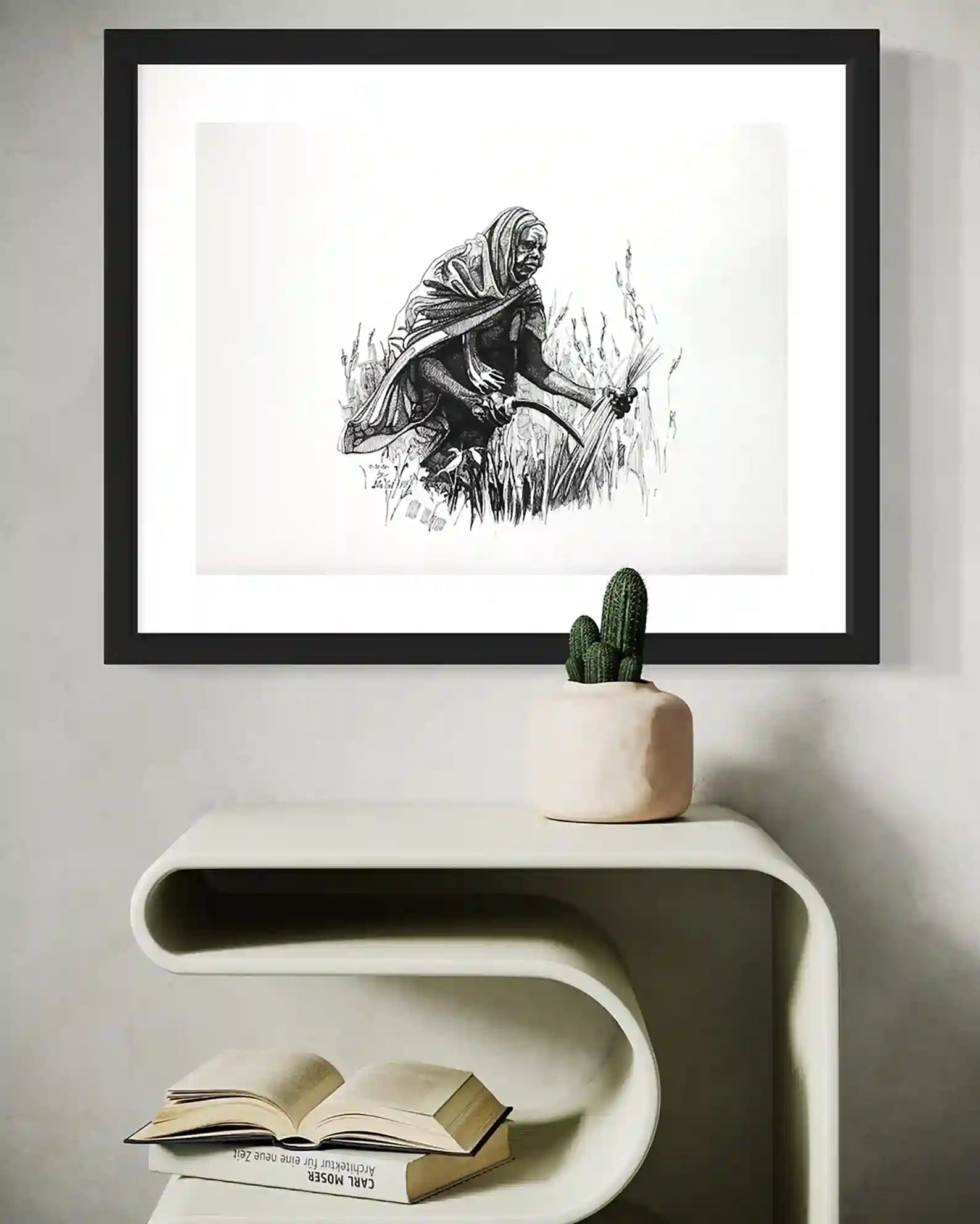 Among the Grasses framed ink painting by Obada Gabir above modern table showing Sudanese woman cutting grass mockup