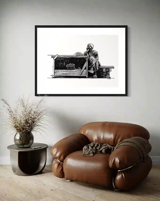 Obada Gabir vegetable seller pen and ink art print in black frame displayed above brown leather chair in modern living room