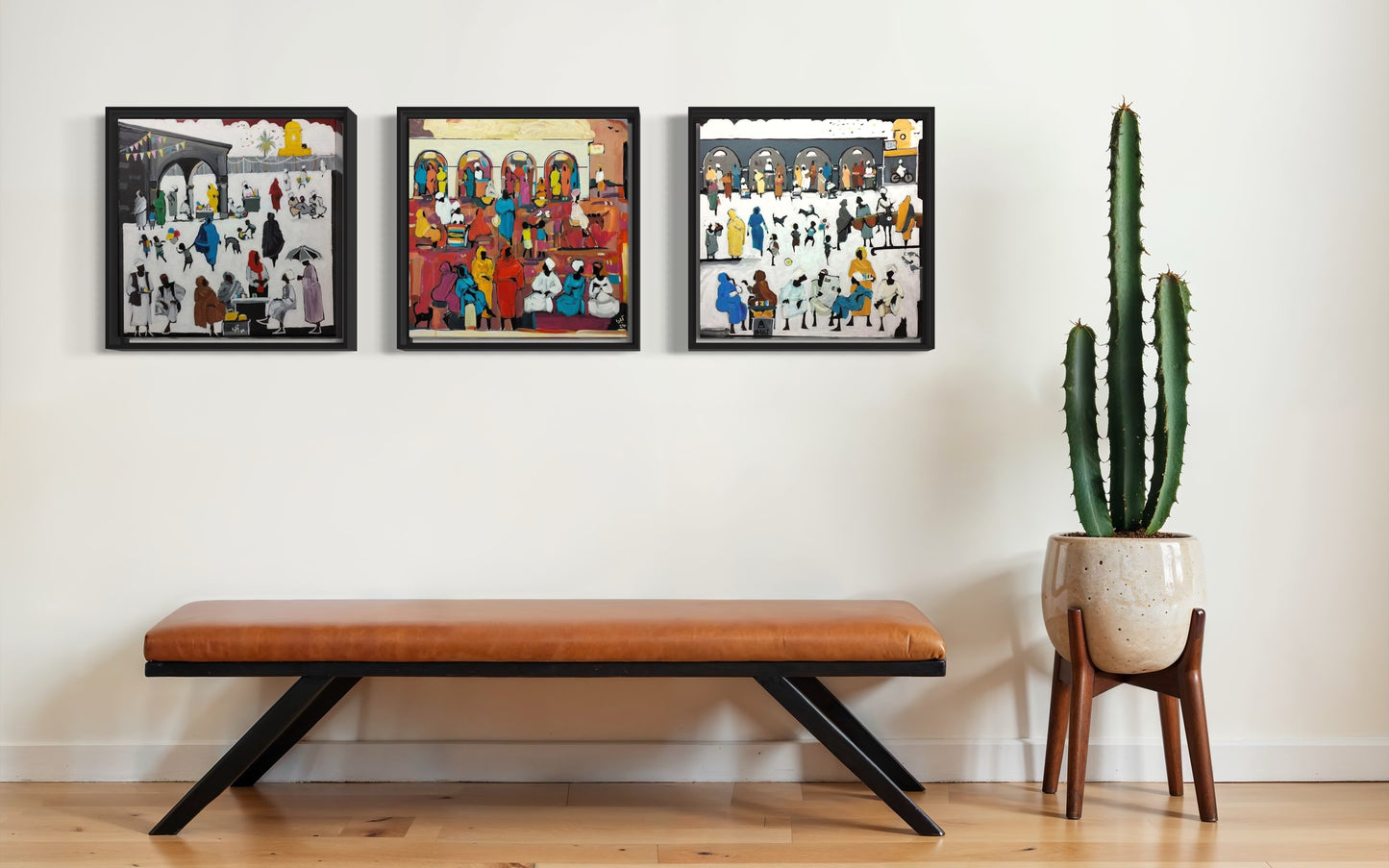 Three colorful paintings above a wooden bench with a cactus in a pot nearby.