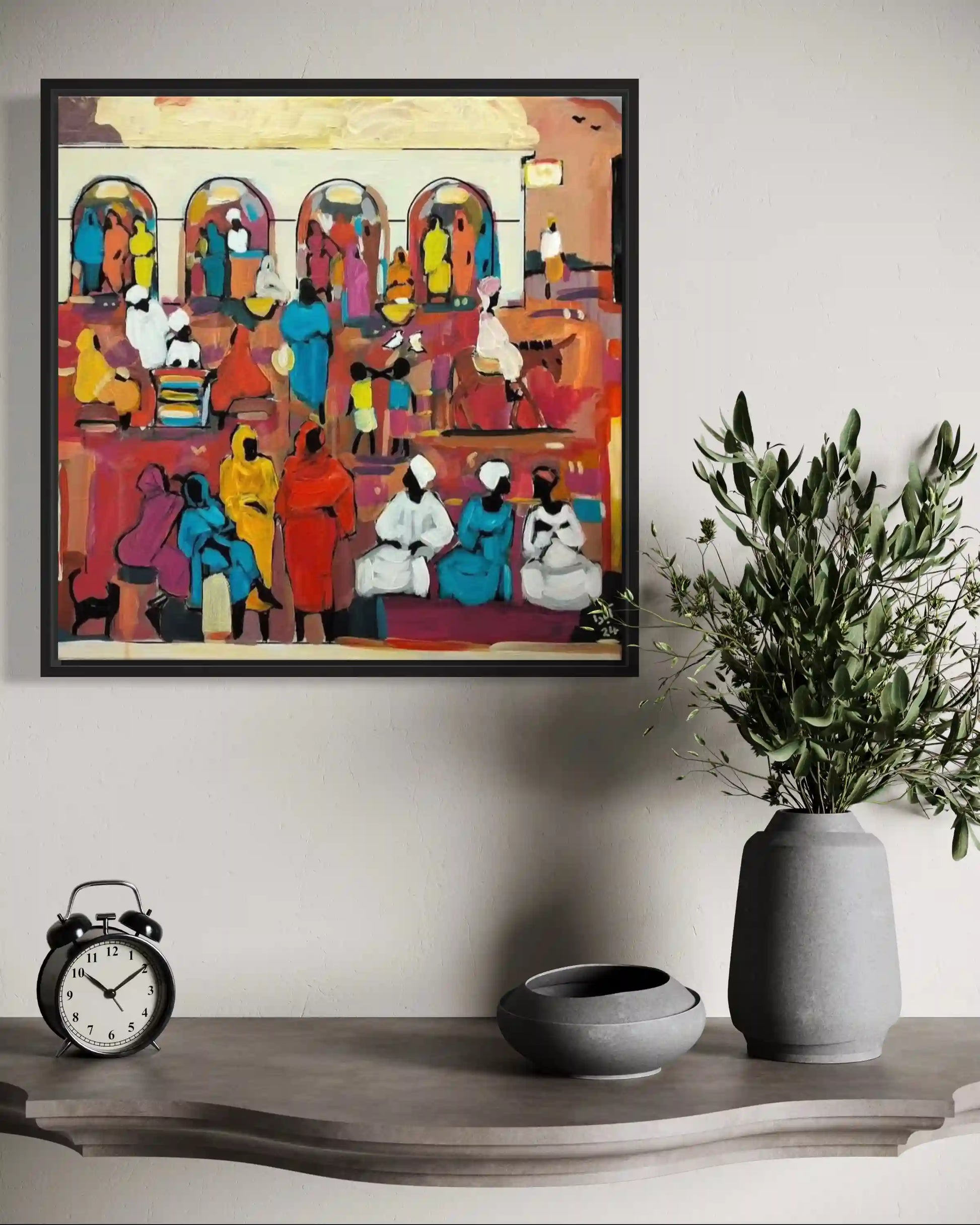 Framed colorful artwork of people in a market scene, above a wooden shelf with a clock and vase.