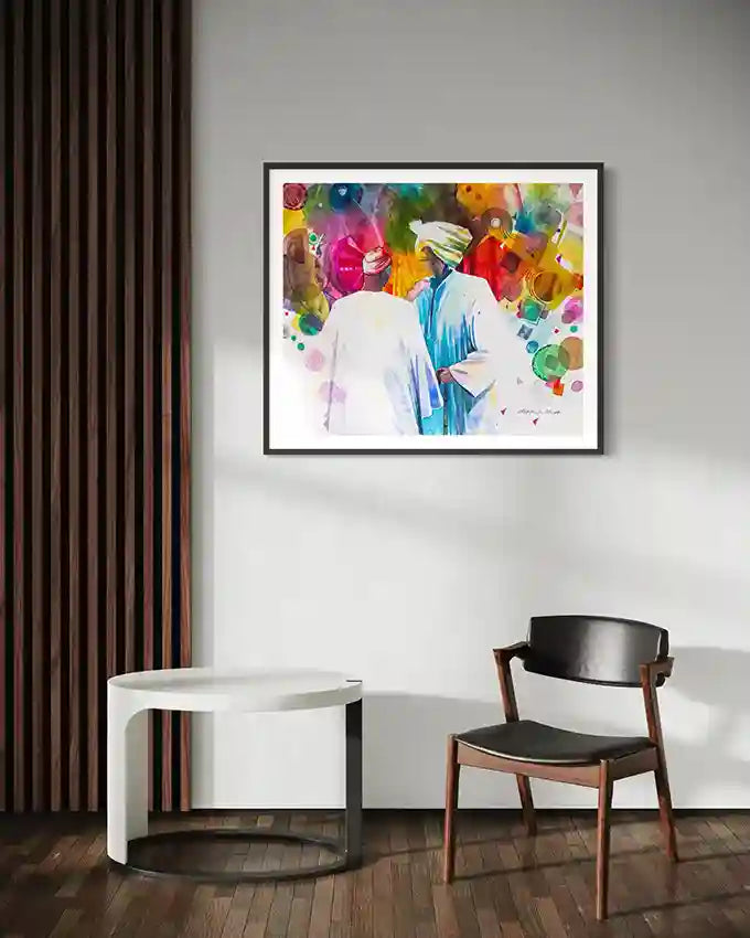 large Colorful abstract framed print of two men by artist Galal Yousif on a wall above a white table and black chair. UAE