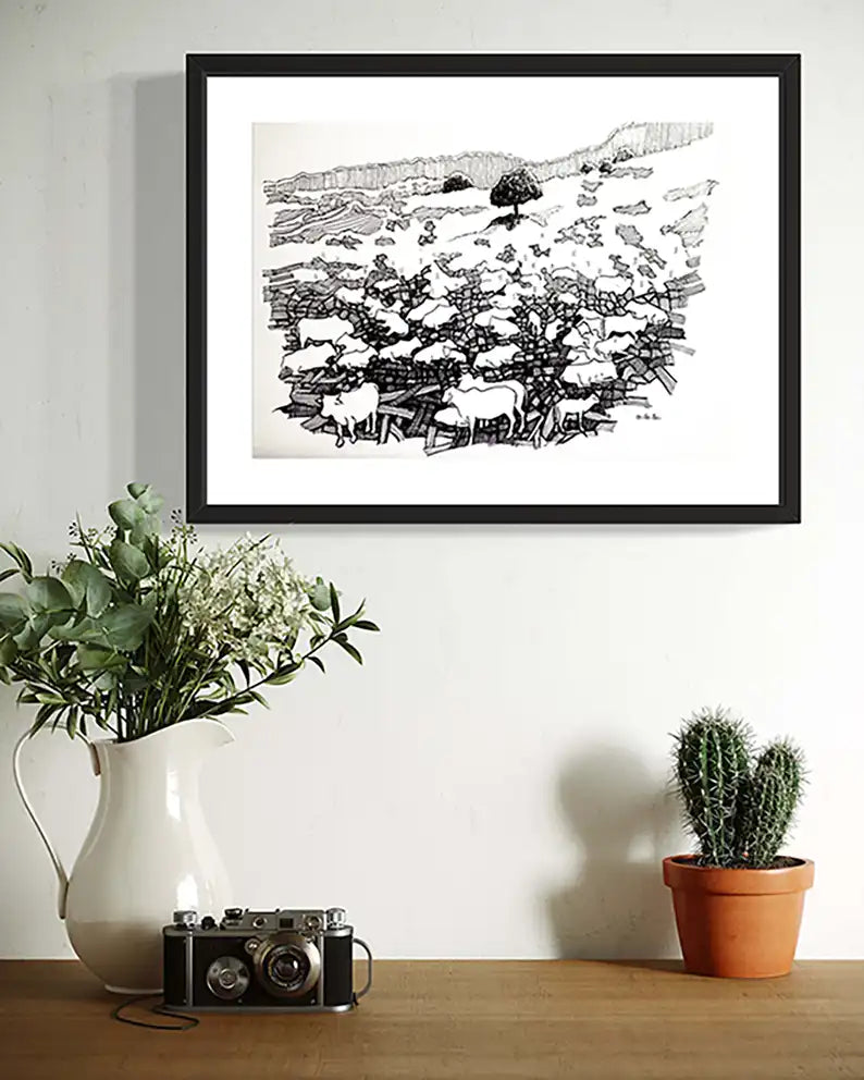 Framed Grazing Ground ink artwork by Obada Gabir displayed on wall above wooden shelf with plants and vintage camera
